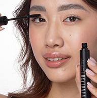 Er wordt gezien hoe een vrouw mascara op haar ogen aanbrengt, terwijl ze het borsteltje voorzichtig vasthoudt terwijl ze haar wimpers accentueert.