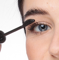 Een vrouw brengt mascara aan met een borstel, waardoor haar wimpers volume krijgen en haar oogmake-up wordt geperfectioneerd.