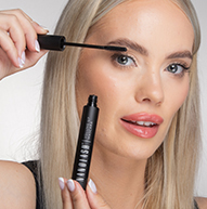 Een vrouw brengt zorgvuldig mascara aan op haar wimpers en houdt het borsteltje van dichtbij voor een perfecte afwerking.
