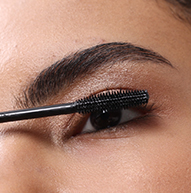 Een close-up van iemand die met een staafje zwarte Nanolash-mascara op de bovenste wimpers aanbrengt.