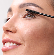 Er wordt een vrouw gezien die mascara aanbrengt met een penseel, waarbij ze zorgvuldig haar wimpers accentueert voor een dramatischer uiterlijk.