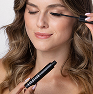 Een vrouw brengt zorgvuldig mascara aan om haar wimpers te accentueren en concentreert zich aandachtig op haar make-uproutine.