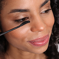 Een vrouw brengt mascara aan op haar oog en laat haar make-upproces zien in een heldere en elegante omgeving.