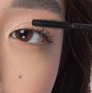 Er wordt een vrouw gezien die mascara aanbrengt met een borsteltje, waarbij ze zich concentreert op haar wimpers om een gedefinieerde en elegante look te verkrijgen.